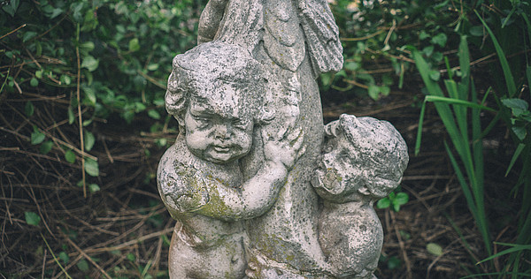 Detail of a stone statue depicting two children. The statue is placed outside and weathered.