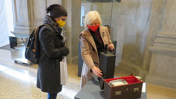 Two people wearing face masks are looking at an object that is placed on a display plinth. 