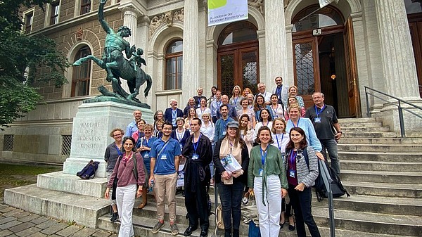 A large group of people stands on the stairs leading up to the Akademie der bildenden Künste Vienna..
