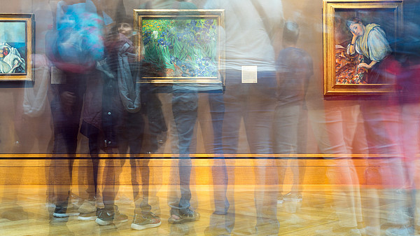 The photographer has used the slow shutter function so that it looks like several people are moving quickly in front of a wall with three pictures on it.