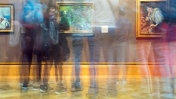  The photographer has used the slow shutter function so that it looks like several people are moving quickly in front of a wall with three pictures on it.