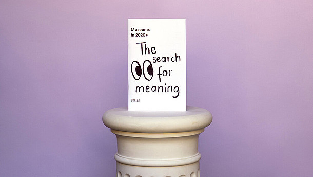  A card is placed on an antique socket, set before a lilac background. The white card reads "The search for meaning". Next to the writing two eyes are drawn in cartoonish style.