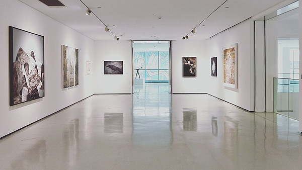 Empty gallery space with white walls, floors and ceiling. Big paintings hang on the walls.
