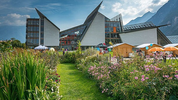 A modern museum building in an alpine landscape is surrounded by a blooming garden.