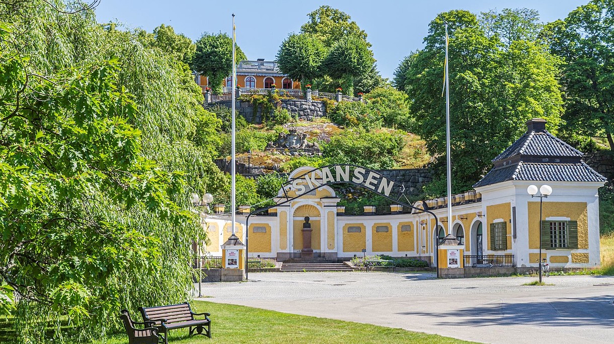 © Skansen, Image: Jonathan Lundkvist Picture of the entrance to an open-air museum. The entrance is yellow and surrounded by green trees.