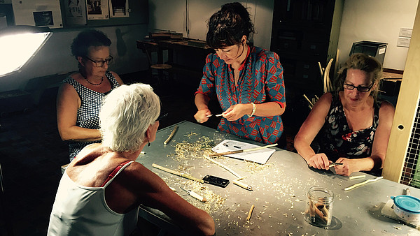 Four women sit around a table to do a wood workshop.