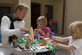 A man helps two children build paper dolls. 