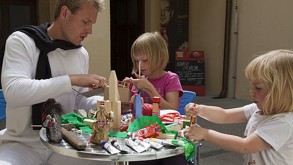 A man helps two children build paper dolls. 