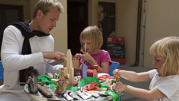  A man helps two children build paper dolls. 
