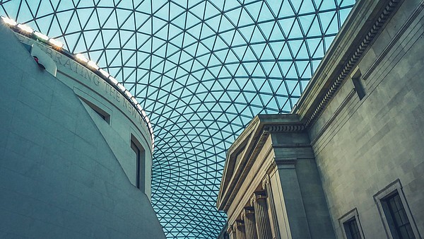This photograph shows the glass ceiling of a museum building. The ceiling connects a modern building on the left and a classical building on the right.