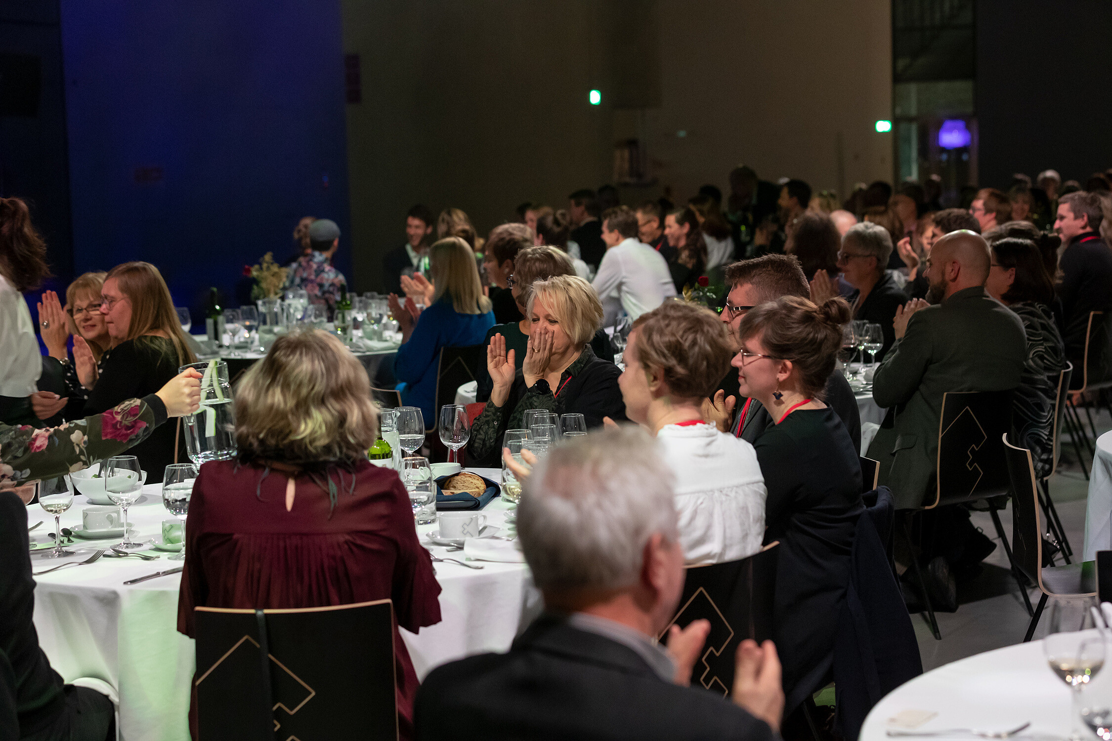 © Image: Arp Karm People are sitting down around round dinner tables. They are clapping their hand. © Image: Arp Karm