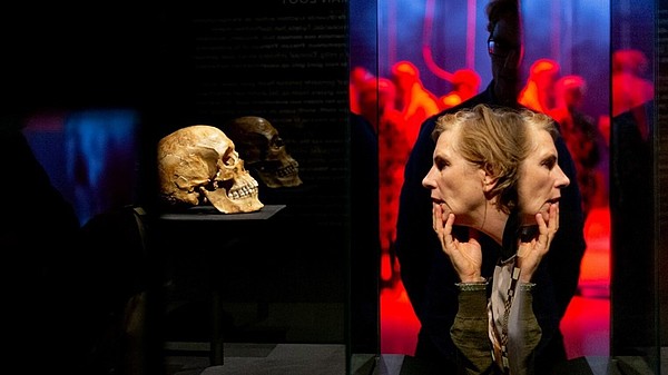 Person in profle looking contemplatively at a human skull that is placed on a small table. 