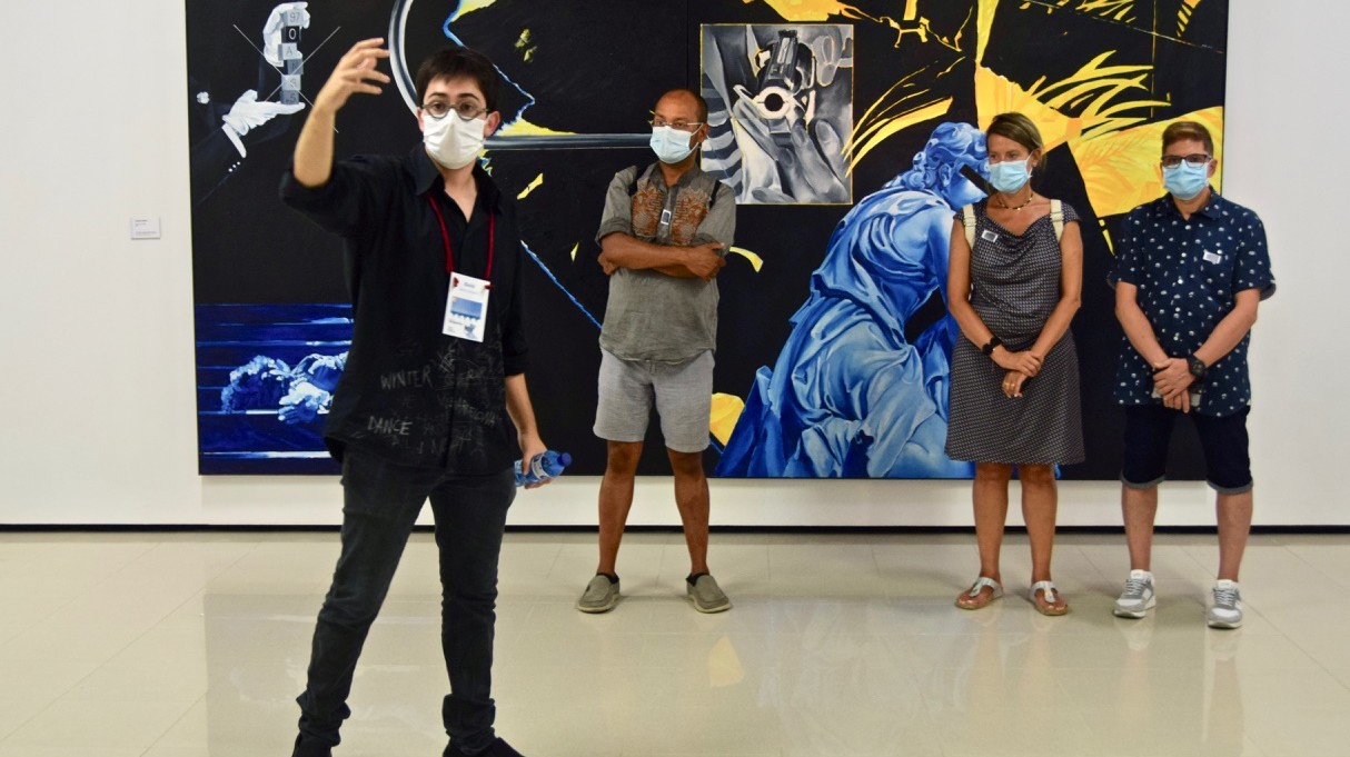 © Arxiu Fotogràfic del Consorci del Patrimoni de Sitges   A man is taking a selfie of himself and three other people standing behind him in front of a big painting. They are all wearing face masks. 