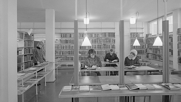  Black and white photo showing four people browsing or reading books in a book shop or library.. 