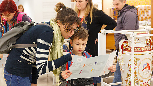 A child is holding a leaflet. An adult next to them is explaing to them.