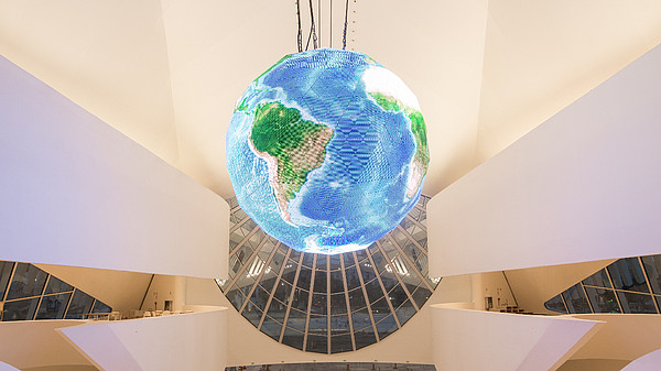 Photo shows a very modern and white building from inside. A big, illuminated globe is hanging from the ceiling.