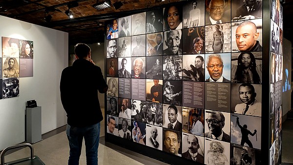 A person with their back to the camera is looking at photo collage that is covering a wall.