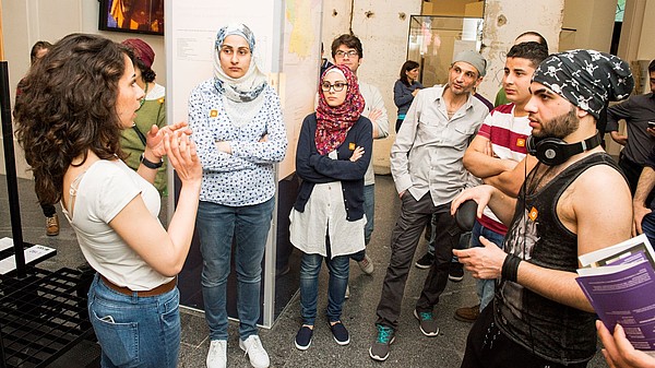 A group of people listen to a museum guide in the middle of an exhibition room.