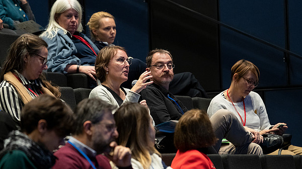 A person sitting in an audience uses a microphone to ask a question. 