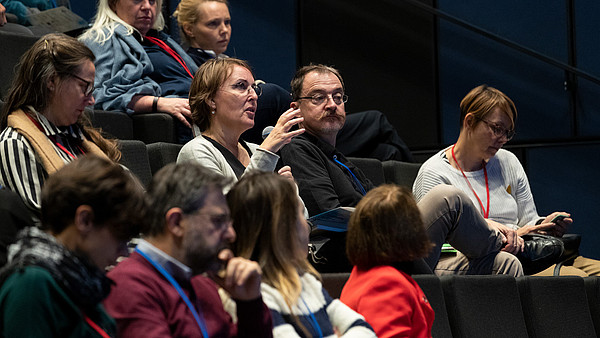 A person sitting in an audience uses a microphone to ask a question. 